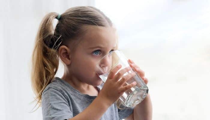 Little girl with pony tails drinking water from a glass