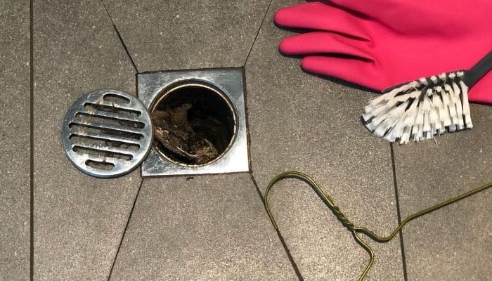 Clogged shower drain with cover removed and coat hanger and red glove